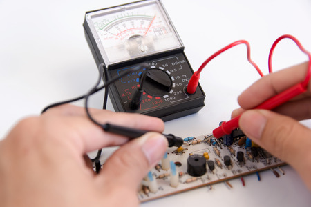 Technician hand with multimeter probes repairing circuit boardの写真素材