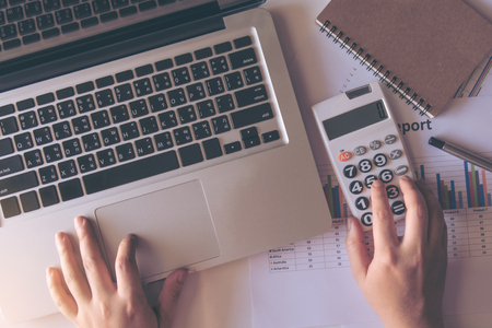 close up woman using calculator and laptop on paper graph data with doing finance at office. top viewの写真素材