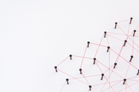 Linking entities, social media, Communications Network, The connection between the two networks. Network simulation on white paper linked together created by black nail and red thread with copy spaceの写真素材