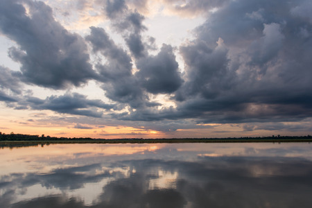 Sunset in the lake. Beautiful sunset behind the storm clouds before a thunder storm above the over lake landscape background. Dramatic sky with cloud at sunset.の写真素材