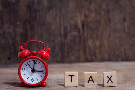 Tax with wooden alphabet blocks and Red alarm clock, on Table dark plank wooden background with copy...