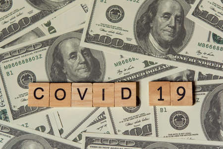 COVID-19 coronavirus with wooden alphabet blocks, on 100 dollar money background with copy spaceの写真素材