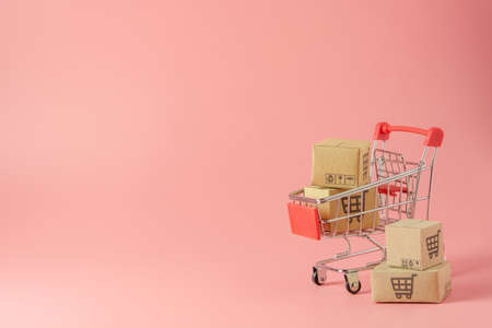 Shopping concept : Cartons or Paper boxes in red shopping cart on pink background. online shopping consumers can shop from home and delivery service. with copy spaceの写真素材