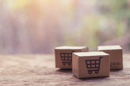 Online shopping - Paper cartons or parcel with a shopping cart  on wood table top. Shopping service on The online web and offers home delivery.の写真素材