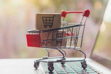 Shopping online concept - Parcel or Paper cartons with a shopping cart  in a trolley on a laptop keyboard. Shopping service on The online web. offers home delivery.の写真素材