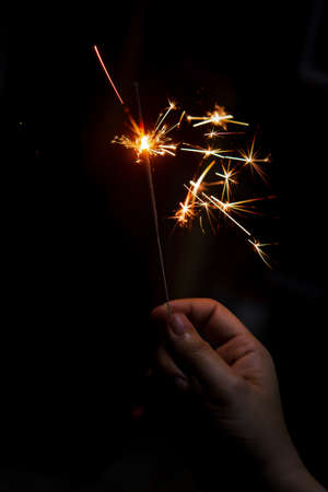 Female hand holding a burning sparkler, Christmas and new year sparkler holiday background
