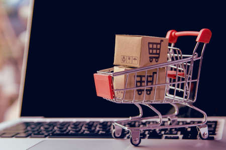 Shopping online concept - Parcel or Paper cartons with a shopping cart   in a trolley on a laptop keyboard. Shopping service on The online web. offers home delivery.の写真素材