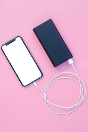 Smartphone charging with power bank on pink background. white screen or blank screen with clipping...