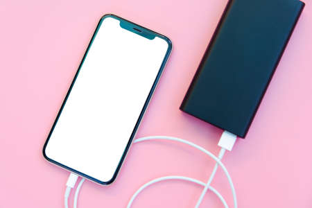 Smartphone charging with power bank on pink background. white screen or blank screen with clipping...