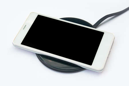 Smartphone charging on a wireless charger on white background. black screen or blank screen with clipping path for copy space. Flat layの写真素材