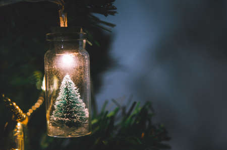 Christmas decoration. Hanging small Christmas tree in glass jar on pine branches christmas tree garland and ornaments over abstract bokehの写真素材