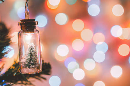 Christmas decoration. Hanging small Christmas tree in glass jar on pine branches christmas tree garland and ornaments over abstract bokehの写真素材