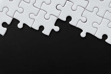 Unfinished white jigsaw puzzle pieces on black background with  copy spaceの写真素材