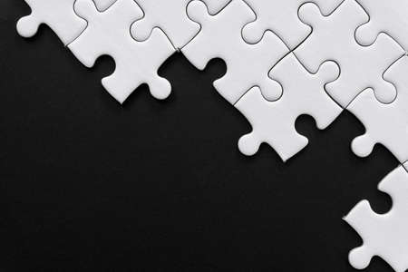 Unfinished white jigsaw puzzle pieces on black background with  copy spaceの写真素材