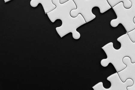 Unfinished white jigsaw puzzle pieces on black background with  copy spaceの写真素材