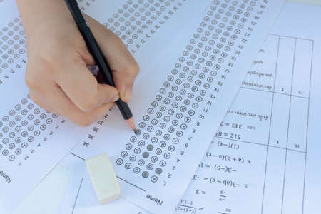 Students hand holding pencil writing selected choice on answer sheets and Mathematics question...