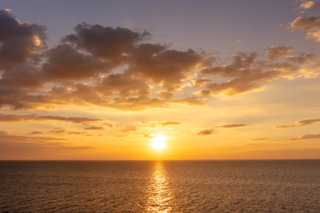 Sunset reflection ocean. beautiful sunset behind the clouds and blue sky above the over ocean landscape backgroundの写真素材