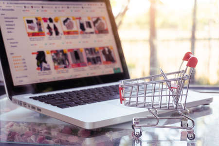 Online shopping concept - shopping cart or trolley and laptop on tableの写真素材