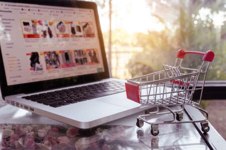 Online shopping concept - shopping cart or trolley and laptop on tableの写真素材