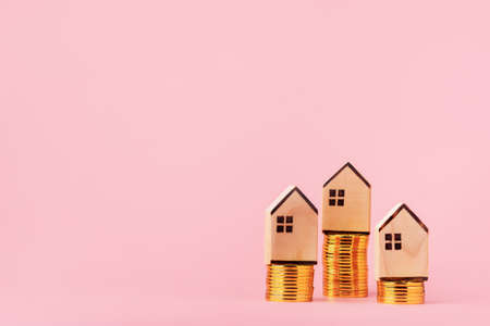 Money saving and investment concept. Wooden houses standing on stacks of coins. on pink background...