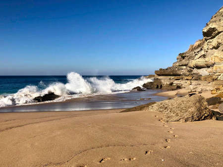 a beach with waves and footsteps in the sand