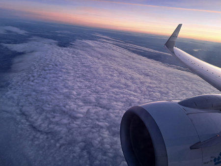 View of the wing of an airplane flying above the clouds at sunsetの写真素材