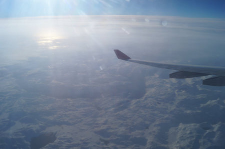 As the airplane ascends, the wing offers a stunning perspective of vast, fluffy clouds blanketing a wintry scene below, illuminated by sunlight filtering through the atmosphere.の写真素材