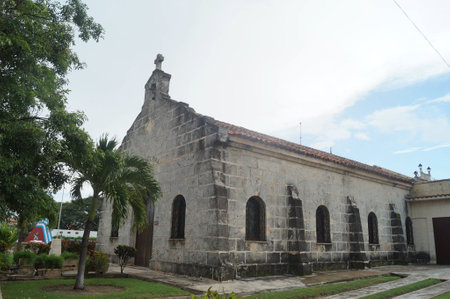 A serene view of a rustic stone church with tall arched windows and a simple cross atop its roof, surrounded by lush greenery and a peaceful atmosphere.の写真素材