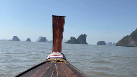 Gently gliding through calm waters, the longtail boat reveals breathtaking limestone islands under a clear sky. The serene atmosphere invites exploration and adventure in nature's beauty.の写真素材