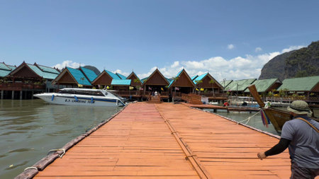 Bright blue skies stretch above a vibrant wooden boardwalk surrounded by picturesque bungalows. People stroll along the pier, enjoying the stunning tropical atmosphere.の写真素材