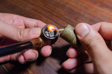 man lighting a tobacco pipe on a wooden table background Soft focus