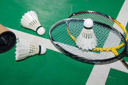 Badminton rackets and white cream badminton shuttlecocks after playing or after games on green floor in indoor badminton court soft focus concept for badminton lovers around the world.の写真素材