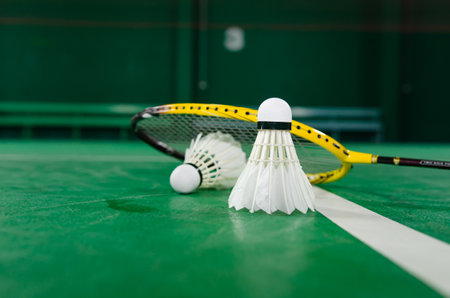 Badminton rackets and white cream badminton shuttlecocks after playing or after games on green floor...