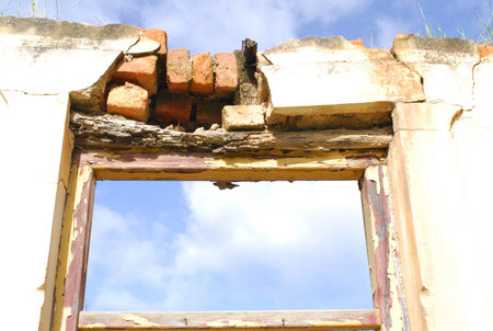 Blue sky shines in through the fanlight above the doorway of a dilapidated house の写真素材