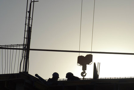 Construction with crane hook and workers in silhouetteの写真素材