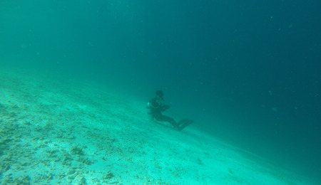 The scuba diver sits on the seabed, in front of the sea abyss.の写真素材