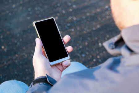 mockup image of the hands of sitting man holding a white mobile phone with a blank screen on the...