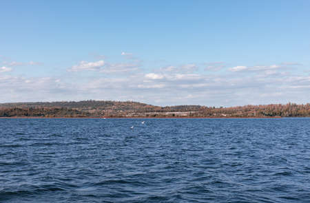 Beautiful Landscape on the sea, Water with a blue sky and some autumn like forest on the landの写真素材