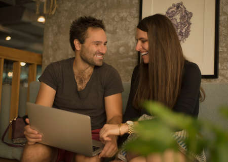 Smiling best friends watching funny videos from network on laptop during free time in cafe interior,couple in love enjoying online shopping choosing items in web store satisfied with prices on saleの写真素材