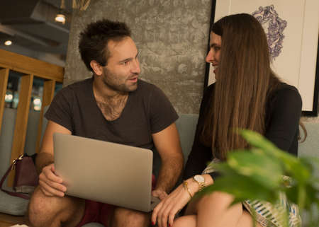 Smiling best friends watching funny videos from network on laptop during free time in cafe interior,couple in love enjoying online shopping choosing items in web store satisfied with prices on saleの写真素材