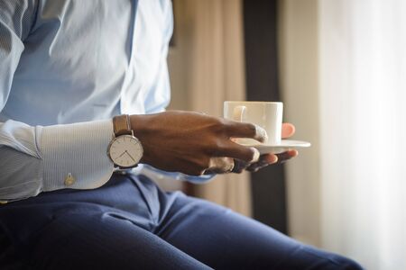 Businessman with watch on his wrist drinking morning coffeeの写真素材