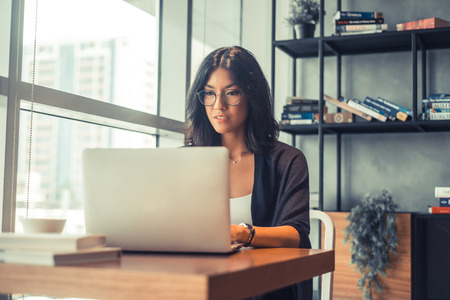 Beautiful business woman is using a laptop and smiling while working in officeの写真素材