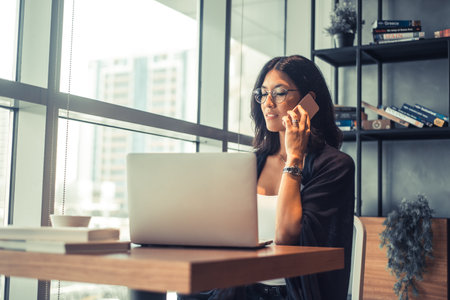 Beautiful business woman is using a laptop and smiling while working in officeの写真素材