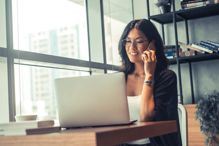 Beautiful business woman is using a laptop and smiling while working in officeの写真素材