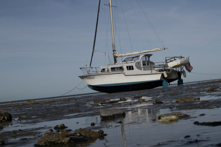 Picture of a boat at low tide standing on the seabed at the coast or Lauwersoog in the Wadden Sea. Some rocks on the foreground. The view does not follow the horizonwhich makes it more dynamic.のeditorial素材