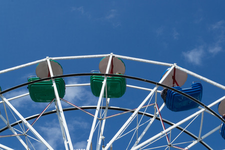 Upper part of ferris wheel with green and blue bowls against blue sky with thin cloudsの写真素材