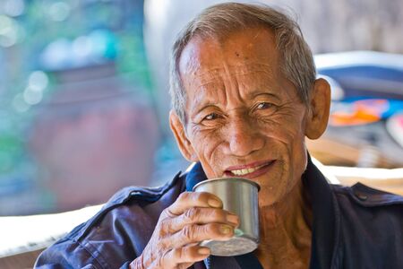 An aged cheerful old man holding a cup of coffeeの写真素材