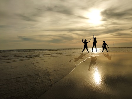 young people jumping on the beach with sunset backgroundの写真素材