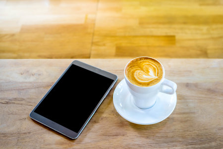 Hot art coffee cappuccino in a cup and smartphone  on wooden table backgroundの写真素材
