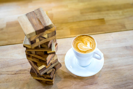 Hot art coffee cappuccino in a cup and Jenga toy on wooden table backgroundの写真素材